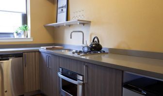 Guest room kitchen in The Fifty Sonesta Select New York, including oven, hob, chopping board, sink, and a small potted plant.