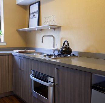 Guest room kitchen in The Fifty Sonesta Select New York, including oven, hob, chopping board, sink, and a small potted plant.