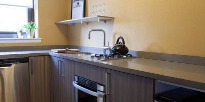 Guest room kitchen in The Fifty Sonesta Select New York, including oven, hob, chopping board, sink, and a small potted plant.