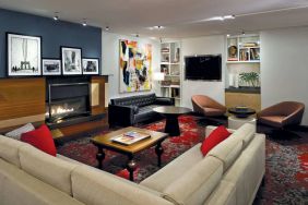 The Den’s lounge in The Fifty Sonesta Select New York features armchairs and sofas, coffee tables and a fireplace, plus a large TV.