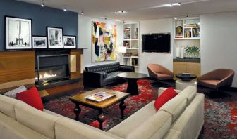 The Den’s lounge in The Fifty Sonesta Select New York features armchairs and sofas, coffee tables and a fireplace, plus a large TV.