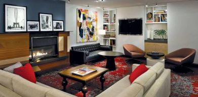 The Den’s lounge in The Fifty Sonesta Select New York features armchairs and sofas, coffee tables and a fireplace, plus a large TV.