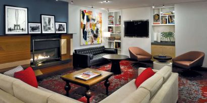 The Den’s lounge in The Fifty Sonesta Select New York features armchairs and sofas, coffee tables and a fireplace, plus a large TV.