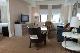 The Benjamin Royal Sonesta New York guest room, featuring chairs, sofa, coffee table, windows, and a television.