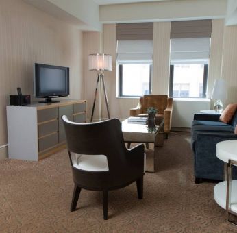 The Benjamin Royal Sonesta New York guest room, featuring chairs, sofa, coffee table, windows, and a television.