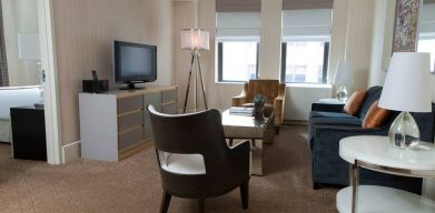 The Benjamin Royal Sonesta New York guest room, featuring chairs, sofa, coffee table, windows, and a television.