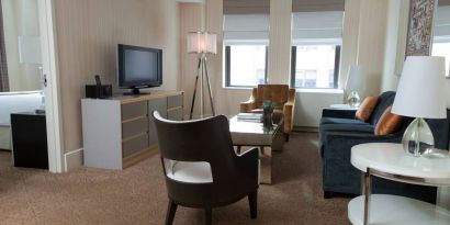 The Benjamin Royal Sonesta New York guest room, featuring chairs, sofa, coffee table, windows, and a television.