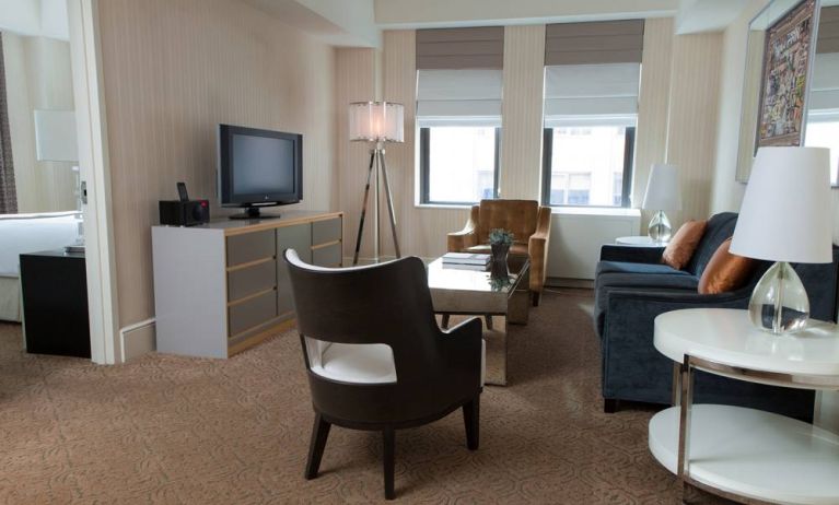 The Benjamin Royal Sonesta New York guest room, featuring chairs, sofa, coffee table, windows, and a television.