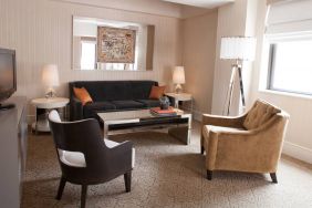 The Benjamin Royal Sonesta New York guest room living area, furnished with coffee table, chairs, TV, and sofa.