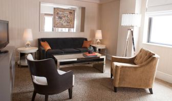 The Benjamin Royal Sonesta New York guest room living area, furnished with coffee table, chairs, TV, and sofa.