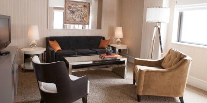 The Benjamin Royal Sonesta New York guest room living area, furnished with coffee table, chairs, TV, and sofa.