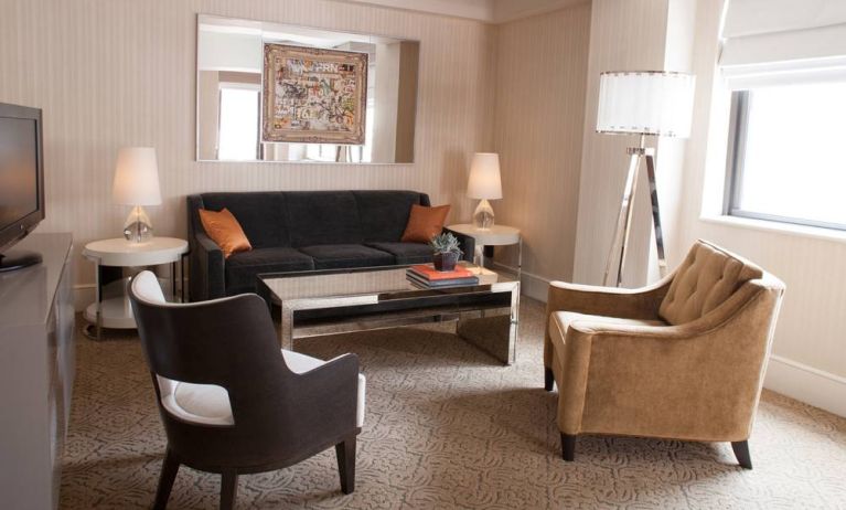 The Benjamin Royal Sonesta New York guest room living area, furnished with coffee table, chairs, TV, and sofa.