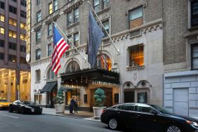 The Benjamin Royal Sonesta New York’s exterior features the hotel’s name on the awning and flag, with a Stars and Stripes flag beside it, and large potted plants.