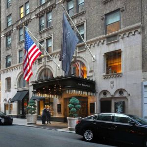 The Benjamin Royal Sonesta New York’s exterior features the hotel’s name on the awning and flag, with a Stars and Stripes flag beside it, and large potted plants.