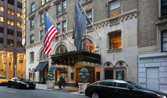 The Benjamin Royal Sonesta New York’s exterior features the hotel’s name on the awning and flag, with a Stars and Stripes flag beside it, and large potted plants.