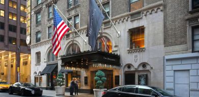 The Benjamin Royal Sonesta New York’s exterior features the hotel’s name on the awning and flag, with a Stars and Stripes flag beside it, and large potted plants.