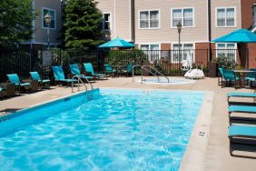 The outdoor pool at Sonesta ES Suites Chicago Waukegan Gurnee ha a nearby hot tub, shaded tables and chairs, and sun loungers and chairs by the side of the pool.