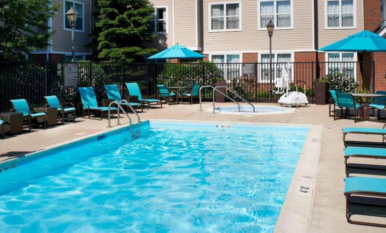 The outdoor pool at Sonesta ES Suites Chicago Waukegan Gurnee ha a nearby hot tub, shaded tables and chairs, and sun loungers and chairs by the side of the pool.