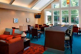 Sonesta ES Suites Chicago Waukegan Gurnee’s lobby lounge has armchairs, chairs, and tall stools, tables of varying sizes, and a wall-mounted TV.