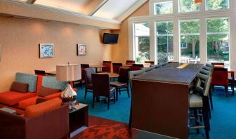 Sonesta ES Suites Chicago Waukegan Gurnee’s lobby lounge has armchairs, chairs, and tall stools, tables of varying sizes, and a wall-mounted TV.