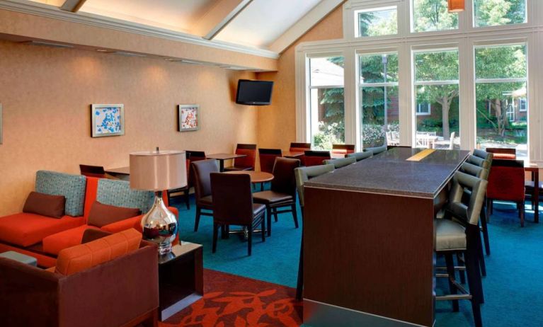 Sonesta ES Suites Chicago Waukegan Gurnee’s lobby lounge has armchairs, chairs, and tall stools, tables of varying sizes, and a wall-mounted TV.