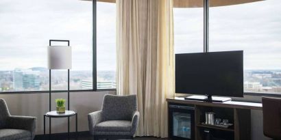 Sonesta Nashville Airport guest room, featuring widescreen television, chairs and a coffee table, and large windows.