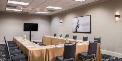 Meeting room in Sonesta Nashville Airport with tables arranged in a U-shape facing  large TV, plus a large artistic photograph of a horse on the wall.