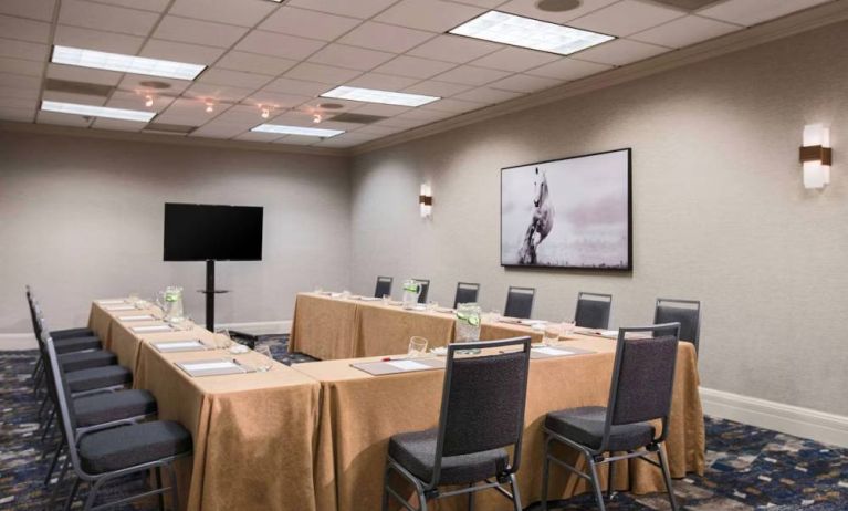 Meeting room in with tables arranged in a U-shape facing  large TV, plus a large artistic photograph of a horse on the wall.