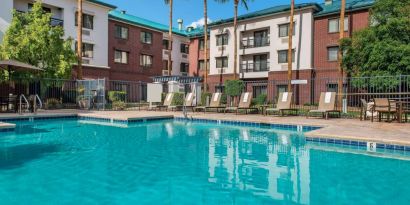 The hotel’s outdoor pool has loungers, as well as a table and chairs, by the side, plus towering trees beyond the fence.