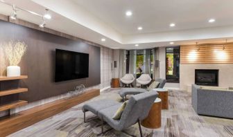 The hotel lobby includes a large, wall-mounted TV faced by a pair of reclined seats, with a fireplace and sofa nearby.