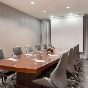 Sonesta Select Tempe Downtown meeting room, featuring long wooden table, a dozen swivel chairs, and a projector screen.