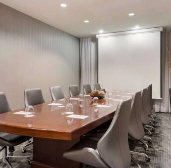 Sonesta Select Tempe Downtown meeting room, featuring long wooden table, a dozen swivel chairs, and a projector screen.