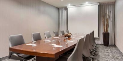 Sonesta Select Tempe Downtown meeting room, featuring long wooden table, a dozen swivel chairs, and a projector screen.