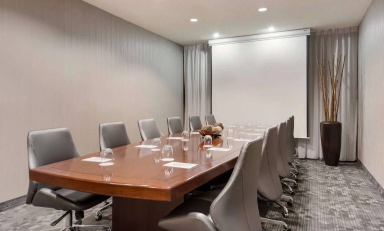 Sonesta Select Tempe Downtown meeting room, featuring long wooden table, a dozen swivel chairs, and a projector screen.