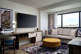 Sonesta Irvine guest room living area, including corner sofa, chair, window, and large, wall-mounted TV.