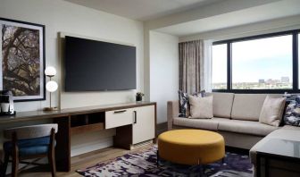 Sonesta Irvine guest room living area, including corner sofa, chair, window, and large, wall-mounted TV.