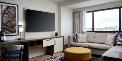 Sonesta Irvine guest room living area, including corner sofa, chair, window, and large, wall-mounted TV.