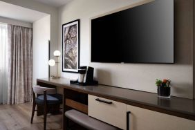 Sonesta Irvine guest room workspace, furnished with desk, chair, and lamp, plus a nearby widescreen TV.