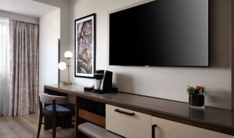 Sonesta Irvine guest room workspace, furnished with desk, chair, and lamp, plus a nearby widescreen TV.