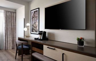 Sonesta Irvine guest room workspace, furnished with desk, chair, and lamp, plus a nearby widescreen TV.