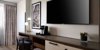 Sonesta Irvine guest room workspace, furnished with desk, chair, and lamp, plus a nearby widescreen TV.