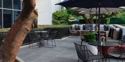 The patio at Sonesta Irvine features sofa seating alongside tables and chairs (shade available), with flowers on each table.