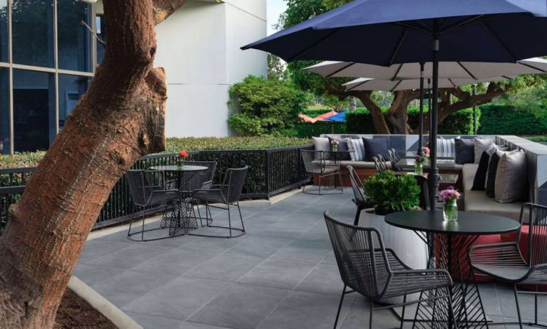 The patio at Sonesta Irvine features sofa seating alongside tables and chairs (shade available), with flowers on each table.