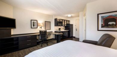 Sonesta Simply Suites Phoenix Tempe double bed guest room, furnished with TV and armchair, plus a workspace desk and chair.