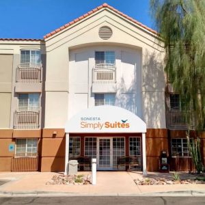 The hotel’s exterior has a pair of benches beneath the covered entranceway, disabled parking spaces nearby, and a towering tree.