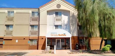 The hotel’s exterior has a pair of benches beneath the covered entranceway, disabled parking spaces nearby, and a towering tree.