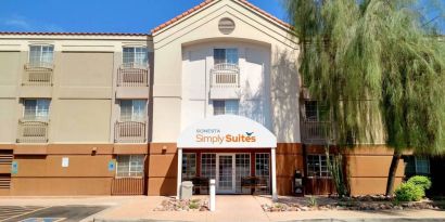 The hotel’s exterior has a pair of benches beneath the covered entranceway, disabled parking spaces nearby, and a towering tree.