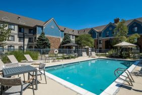 The hotel’s outdoor pool features tables and chairs, with shade available, and sun loungers by the side, with greenery beyond the fence.