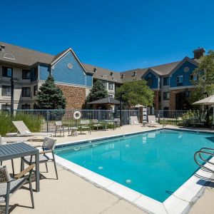 The hotel’s outdoor pool features tables and chairs, with shade available, and sun loungers by the side, with greenery beyond the fence.