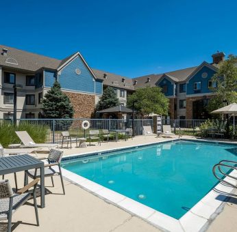 The hotel’s outdoor pool features tables and chairs, with shade available, and sun loungers by the side, with greenery beyond the fence.